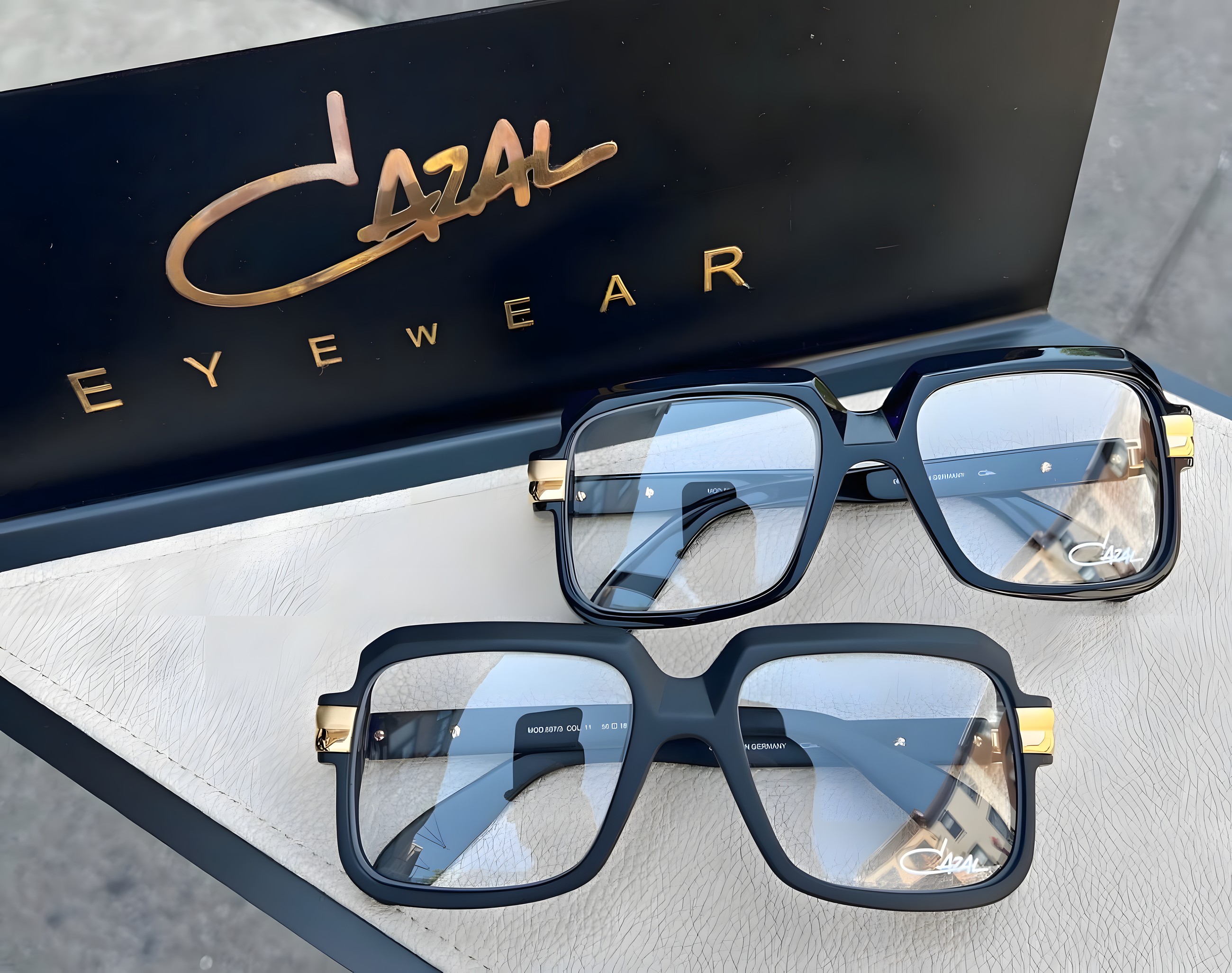 Two Cazal square-frame glasses on a grey leather surface